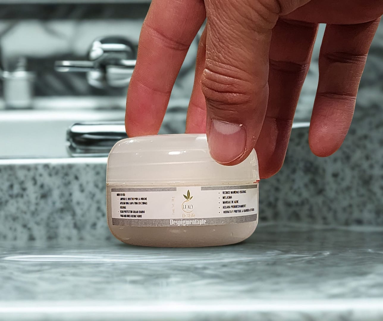 Una mano abriendo crema cicatrizante con ozono sobre un lavabo de baño, mostrando el producto en un entorno de uso diario.
