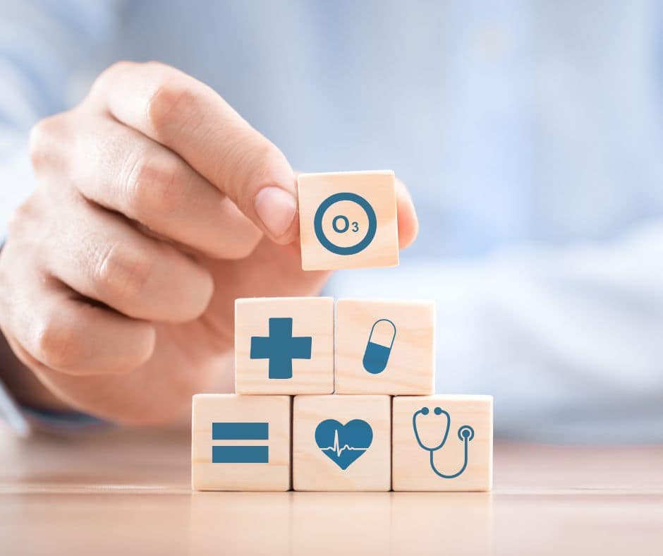 Una mano colocando un bloque de madera con el ícono de ozono (O3) sobre una pila de bloques que representan salud y medicina. Simboliza los beneficios del ozono en la salud.